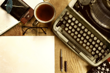 A typewriter and coffee on a desk.
